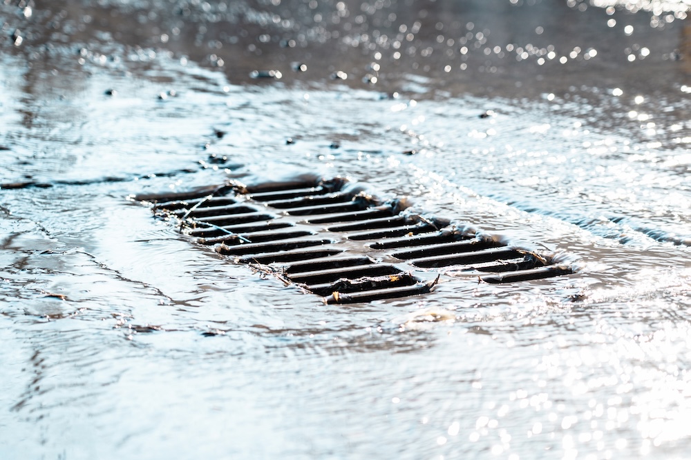 The grate of the storm sewer during rain as the water drains into the drain underneath the street
